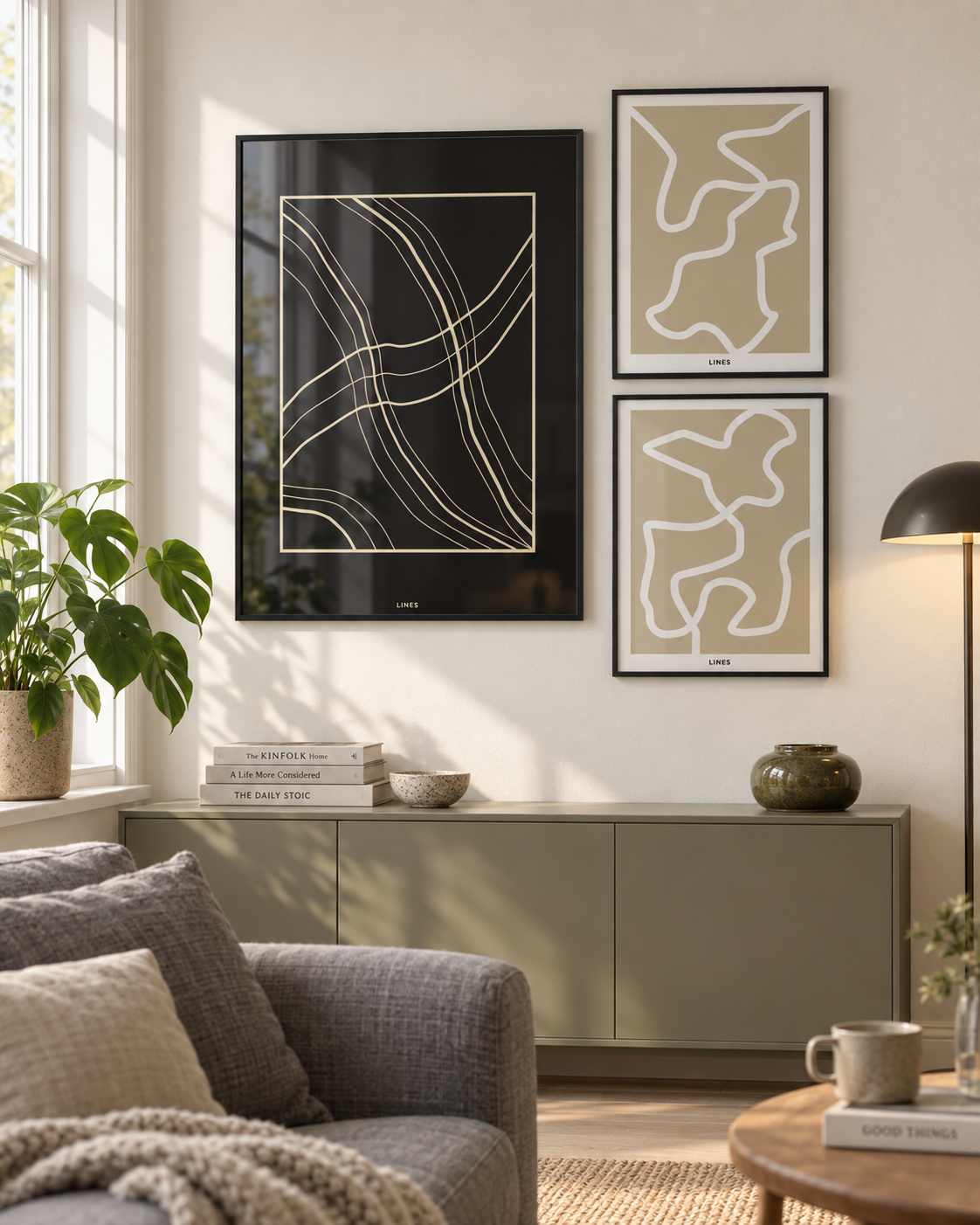 Lines billedvæg med en stor mørk plakat og to mindre grafiske plakater i sorte aluminiumsrammer i en dansk stue.