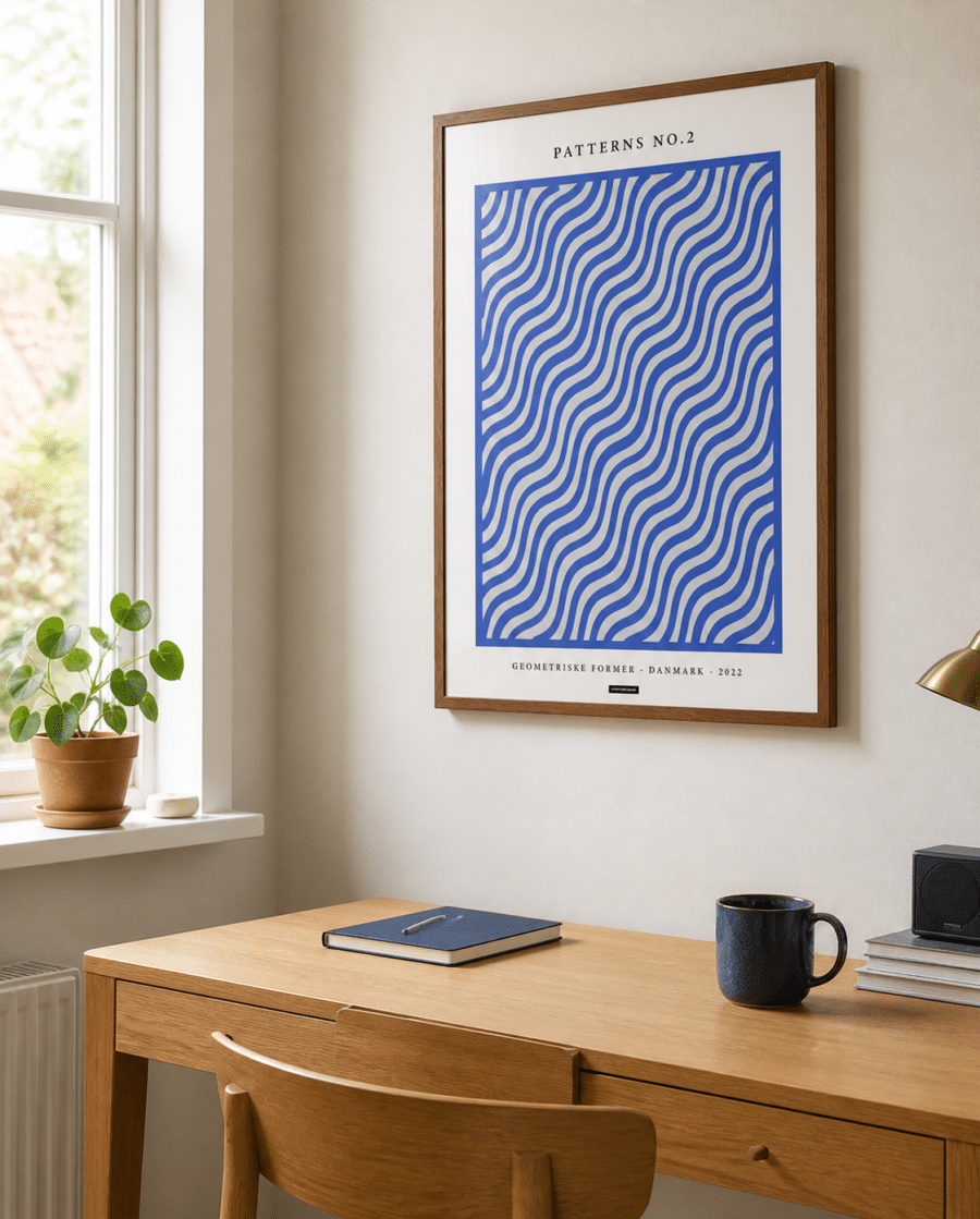 Patterns No.2-plakaten med blå bølger i en varm træramme hænger på en lys væg i et naturligt dansk hjemmekontor med skrivebord og dagslys.