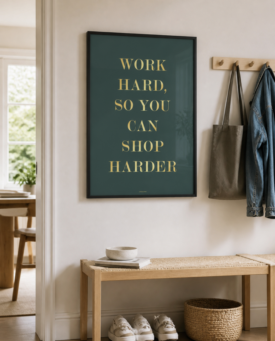 SHOP HARDER plakat i sort ramme i en lys nordisk entre med bænk, knager og naturligt dagslys.